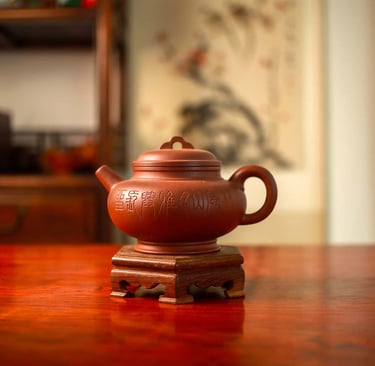 A brown Yixing teapot engraved with designs is placed on a wooden stand