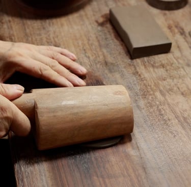 A person using a wooden tool to pound clay, with more clay nearby