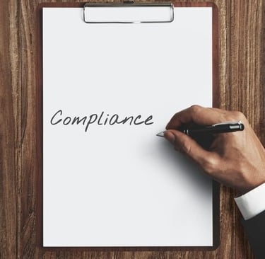 a person writing the word'compliance on a clipboard