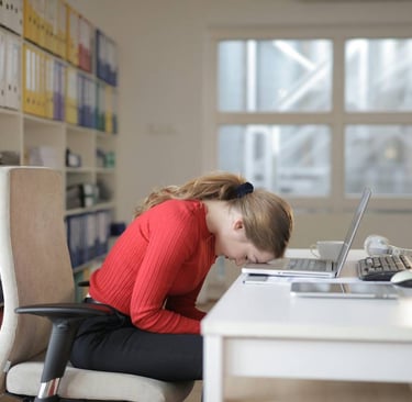 Femme assise à son bureau, penchée vers l’avant, montrant une grande fatigue mentale et physique au travail