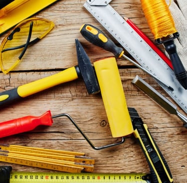 Collection of construction hand tools including a hammer, saw, and ruler on a wooden workbench.