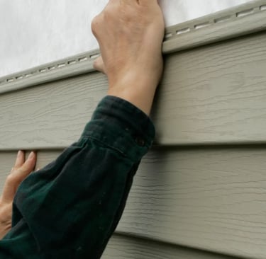 A contractor installs vinyl siding panels on a residential home exterior.