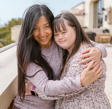 une femme et une jeune fille trisomique se serrent dans les bras et sourient.