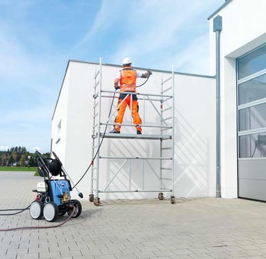 Un ouvrier sur un échafaudage utilise un nettoyeur haute pression pour nettoyer un bardage