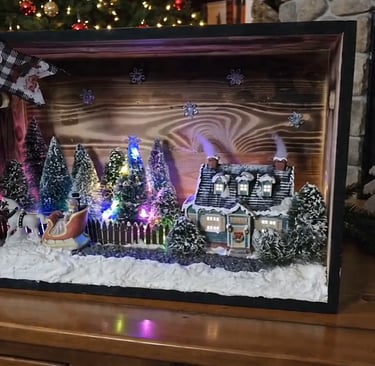 Handcrafted light-up Christmas shadow box featuring a winter village scene with Santa in a sleigh near a fireplace.