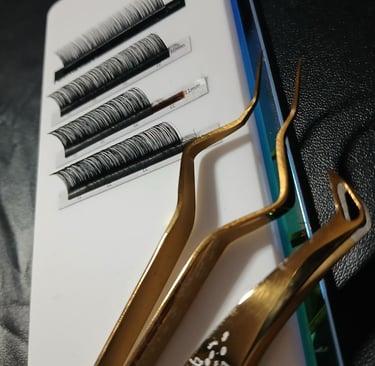 Professional gold lash tweezers next to a tray of individual eyelash extensions for lash artists.