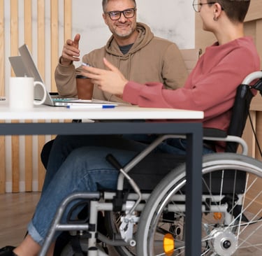 NDIS participant in a wheelchair having a discussion with a support worker at a desk