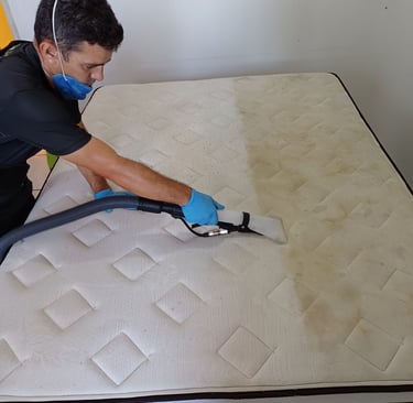 a man in a black shirt and blue gloves cleaning a mattress