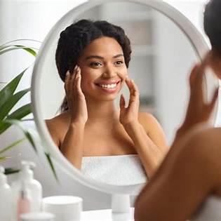 Black woman smiling gently at her reflection in a mirror, radiating self-acceptance, hope, inner joy