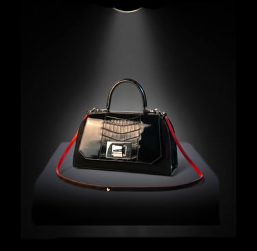 Elegant black crocodile leather handbag with a red shoulder strap illuminated by a spotlight.