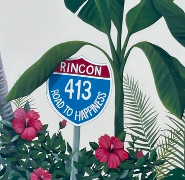 Mural of a Rincon 413 Road to Happiness sign surrounded by tropical hibiscus flowers and banana leaves.
