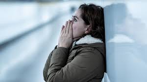 a woman in a brown jacket is holding her hands to her face