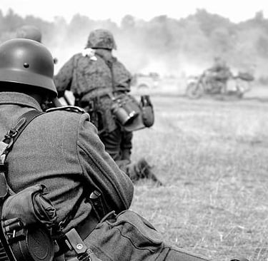 Black and white photo of World War II reenactors in vintage military uniforms with gear during a field battle.