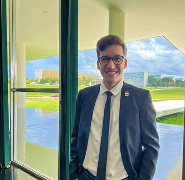 Izaque Costa, homem branco de terno e gravata, sorrindo em pé diante de uma janela.