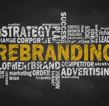 A hand drawing a business rebranding word cloud on a chalkboard with keywords like strategy, advertising, and development.