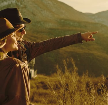 a woman in a hat and a backpack pointing at a mountain