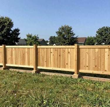 A light brown wooden privacy fence installed in a grassy backyard under a clear blue sky.