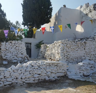 aA whitewashed chapel within a  stone wall with celebration flags 