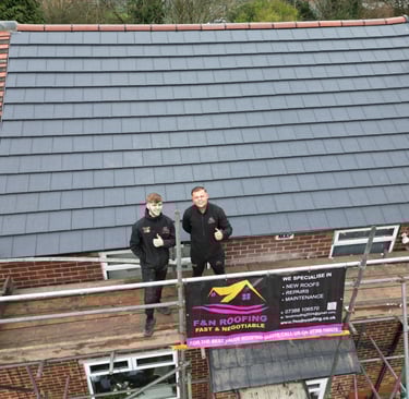 Professional roofing contractors standing on scaffolding after completing a modern grey tile roof installation.