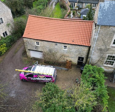 Aerial view of a roofing contractor van parked outside a stone building with a terracotta tile roof.