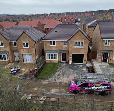 A roofing company van parked in front of a new build brick house on a modern residential construction site.