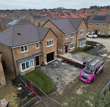 New build brick houses on a modern housing estate with a pink roofing contractor van parked in the driveway.