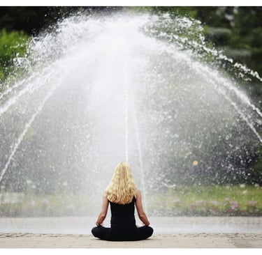 Une femme assise devant une fontaine en position de méditation.