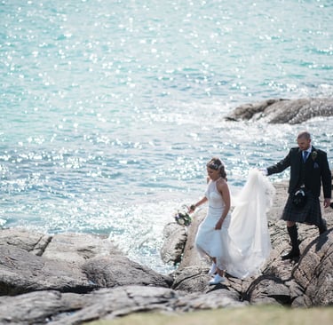 a bride and groom walking down a rocky beach
