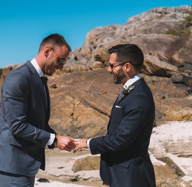 a man in a suit and tie on a beach exchanging rings