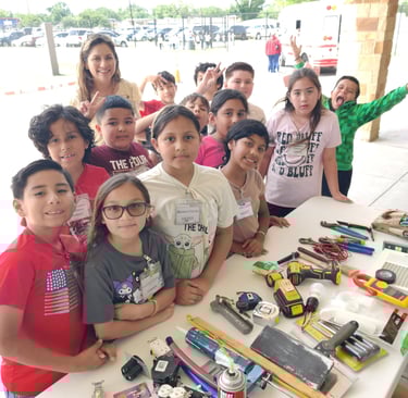 students are around a table with home remodel tools and material for them to see touch & questions