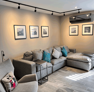 Sala moderna con sofá gris en L, cuadros en blanco y negro y lámparas tipo riel | KARÄNA