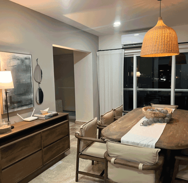 Comedor cálido con mesa de madera, sillas con cojín claro y lámpara colgante de mimbre | KARÄNA