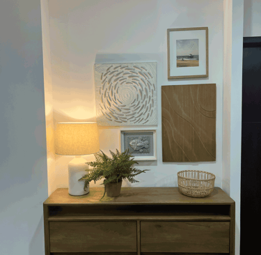 Mueble de recibidor con lámpara cálida, plantas y galería de arte mural en tonos neutros | KARÄNA