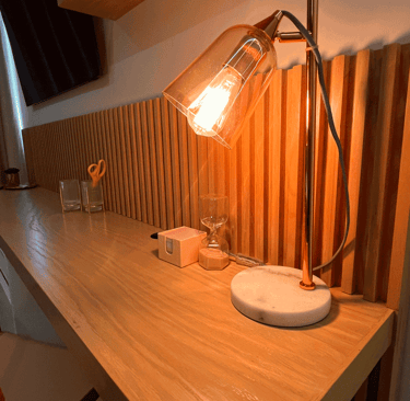 Escritorio de madera con iluminación cálida, lámpara moderna y detalles decorativos | KARÄNA