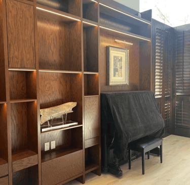 Estantería de madera iluminada con piano cubierto al fondo | KARÄNA