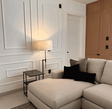 Sala con paneles blancos decorativos, sofá beige tipo chaise lounge y acentos en negro | KARÄNA
