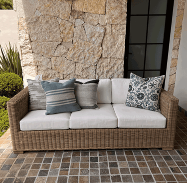 Terraza con sofá tejido, cojines decorativos y muro de piedra natural con vegetación | KARÄNA