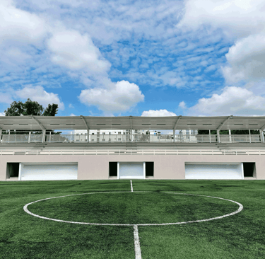 Gradas con techo blanco sobre cancha de pasto sintético | KARÄNA