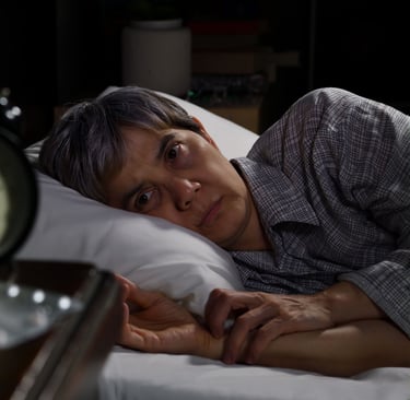 Sleepless person with insomnia lying in bed at night next to an alarm clock and medication.