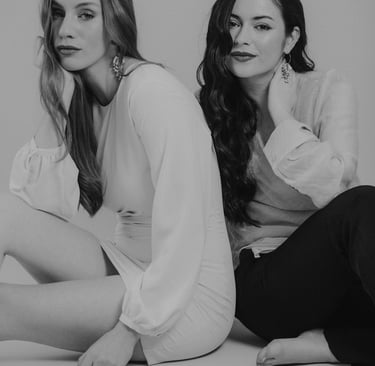 two women sitting on the floor in front of a white wall