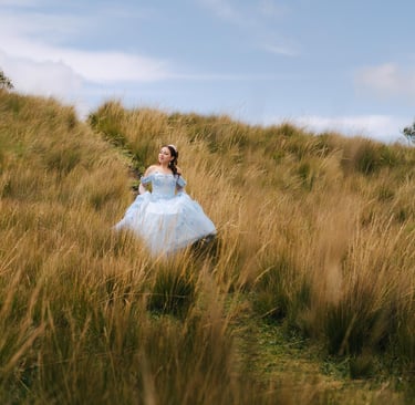 Quinceañera con vestido celeste en un pradp con paja y un cielo azul en Quito Ecuador
