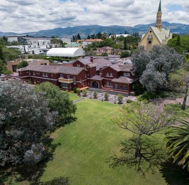 Fotografía aérea de gran casa religiosa de color rojo rodeada de hermoso  jardín verde en Quito Ecuador