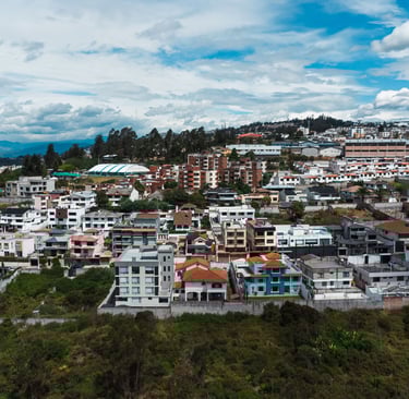 Foto aérea hecha con dron de una pequeña montaña llena de casas y edificios con el cielo azul en Ecuador