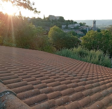 Vue sur une toiture traditionnelle à Volx (Alpes-de-Haute-Provence) avec en arrière-plan le village et son clocher, futur sit