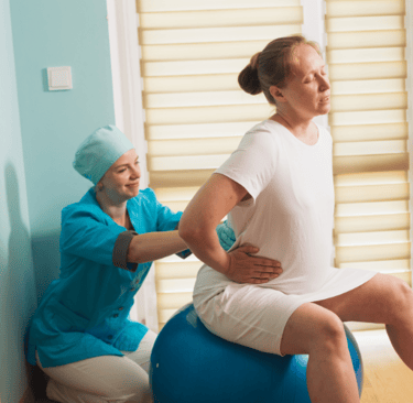 une femme enceinte sur un ballon faisant des exercices avec une sage-femme pendant la grossesse