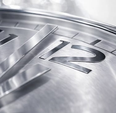 Close-up of a silver luxury watch face with metallic hands pointing towards the number twelve.