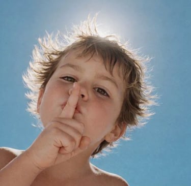 A young child holding a finger to their lips in a hush gesture for confidentiality