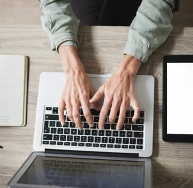 Professional person typing on a laptop at a wooden desk with a digital tablet and notebook.