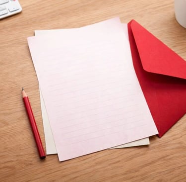 Blank lined stationery paper with a red envelope, pencil, and coffee mug on a wooden desk.
