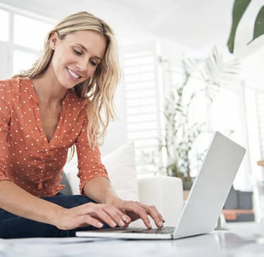 Smiling woman working on a laptop at home in a bright living room.